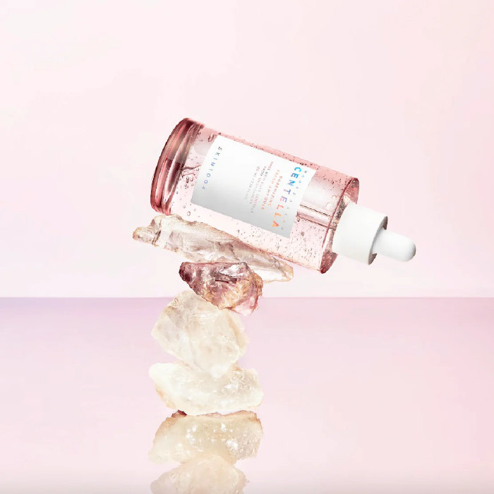 Skincare dropper bottle with crystals on a pink background