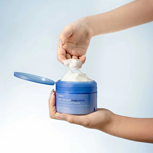 Person holding a blue jar of scalp mask with white cream, against a light gray background