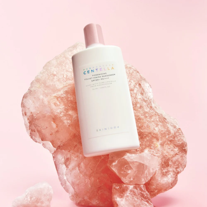 Skincare bottle labeled 'Centella' on a pink stone with a soft pink background
